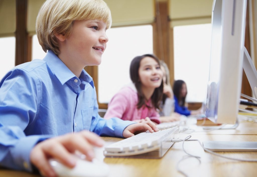 Young boy using computer in classroom with students in background