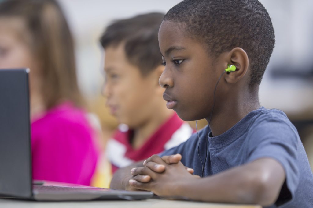 A multi-ethnic group of elementary age children are working on individual laptops in the computer lab.